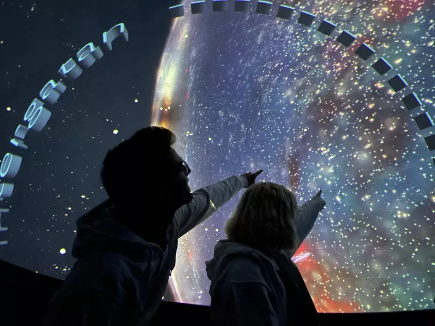 Two students in profile pointing at an image of the galaxy. photo.